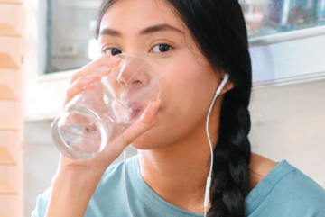 Girl with brain and white headphones drinking glass of water