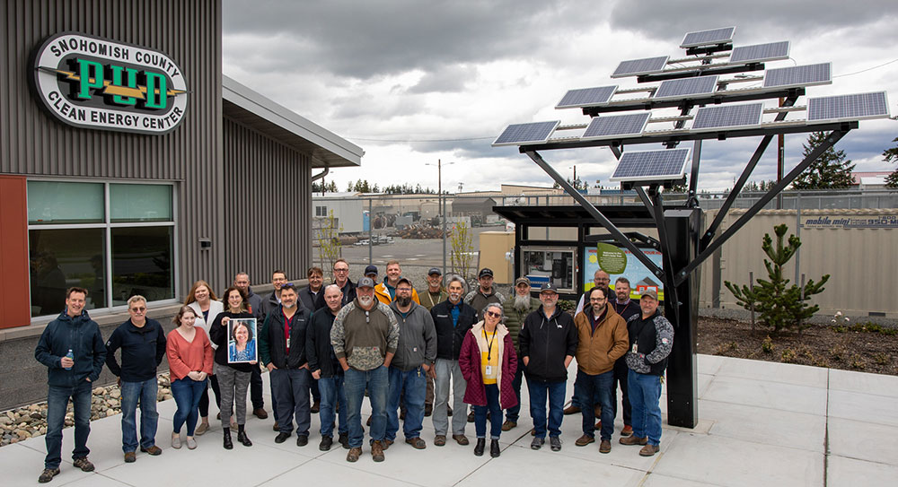 A crowd of smiling people stands next to the solar tree at the Arlington Microgrid