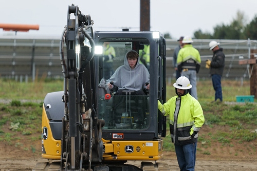 A student works the controls of a backhoe as a PUD worker stands by to assist