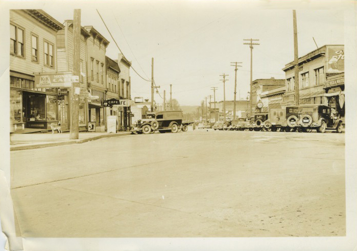 An unpaved road with 1920s-30s vehicles and charming buildings