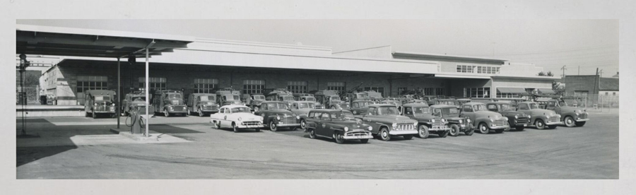 Exterior of the PUD Service building in the 1950s shows cars and line trucks neatly parked
