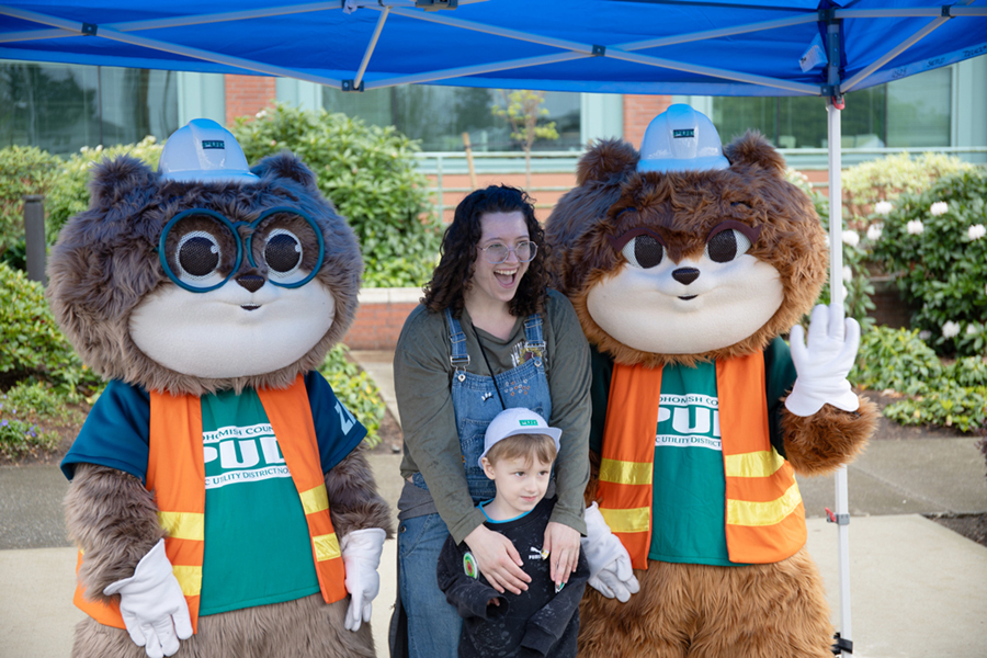 Zip and Zap pose with a smiling mother and child under a blue awning