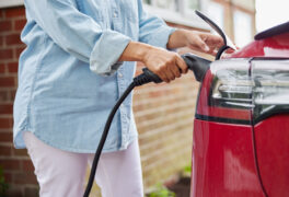 A woman in a light denim top unplugs her electric vehicle from a home charger