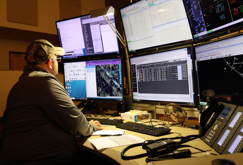 A grid operator reviews six large screens at his desk in the Energy Control Center