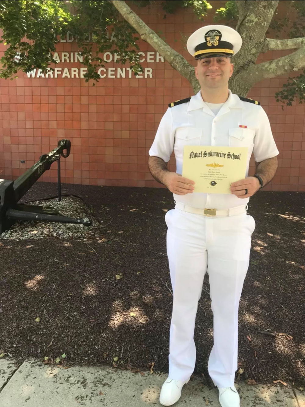 Young naval officer holding certificate in front of official building