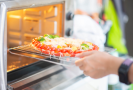 Babaeng naglalagay ng matingkad na kulay na pizza na may maraming gulay sa toaster oven