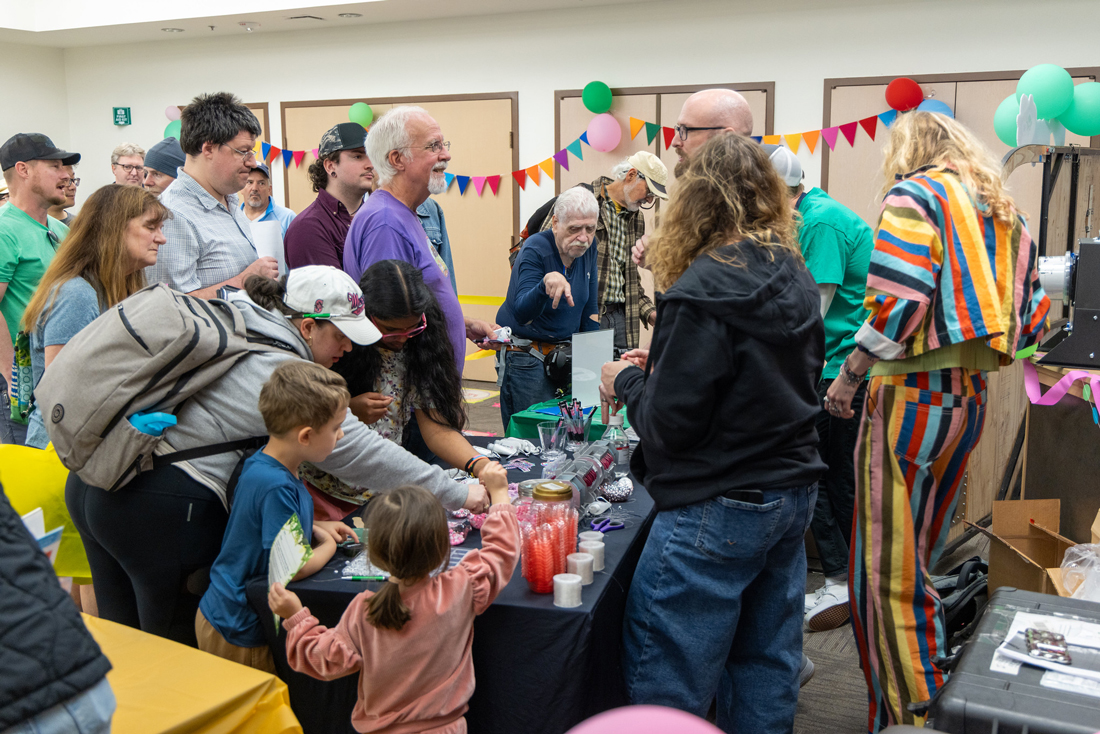一群人坐在装饰着气球和彩带的房间里，与桌子后面的代表交谈。