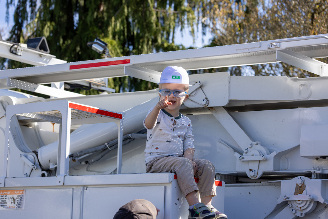 一个戴着眼镜的快乐小男孩戴着 PUD 玩具渔夫帽，坐在高高的运输车上，指着镜头微笑。 