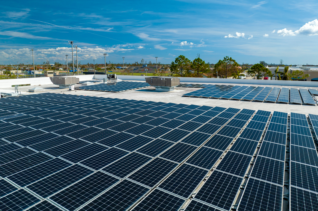 Large rooftop with many solar panels with sun peeking over rooftop