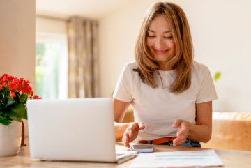 Long haired relaxed woman using computer to pay electric bill, in sunny room